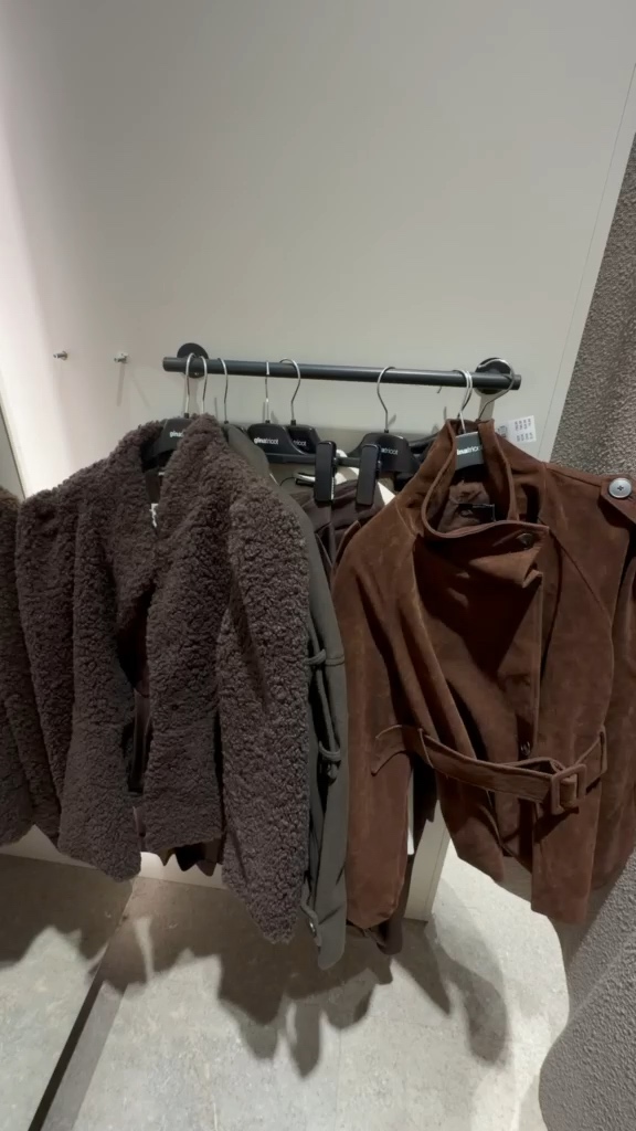 Bruna och grå jackor samt andra plagg på galgar i ett provrum
